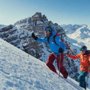 Skitouren-Gruppe auf schneebedecktem Berg mit Gipfel und Bergkette im Hintergrund