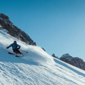 Skifahrer fährt eine steile Schneeabfahrt mit Felsen im Hintergrund hinab