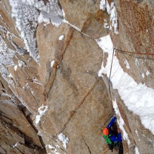 Kletterer in roter und blauer Ausrüstung an schneebedeckter Felswand