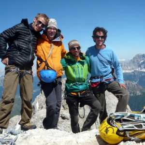 Fünf Personen in Wanderausrüstung posieren auf einem Berggipfel mit Bergpanorama im Hintergrund